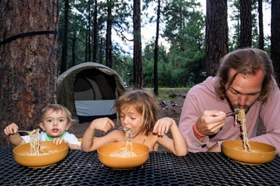 a man and two children eating spaghetti from bowls