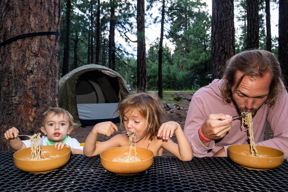 a man and two children eating spaghetti from bowls