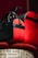 Two stylish bags with black and red leather accents are elegantly displayed on a patterned surface. The bags feature sleek designs with prominent black straps and zippers. The red sections have a glossy finish with a script-like embellishment.