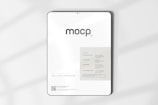 A digital mockup featuring a tablet with a minimalistic design. The screen displays a sleek interface with the word 'mocp' prominently at the top. Below it, there's information about features such as very realistic output and fully editable resolution. The background is clean and white, accented by soft shadows.