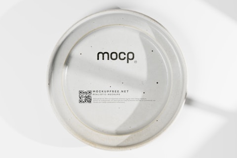 A ceramic plate with a matte finish features the text 'mocp' at the center. Below, there is a QR code and the text 'MOCKUPFREE.NET' followed by smaller additional text detailing its purpose and availability for free commercial use. The plate has a smooth surface with minimal dark speckles throughout.
