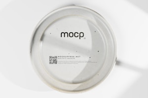 A ceramic plate with a matte finish features the text 'mocp' at the center. Below, there is a QR code and the text 'MOCKUPFREE.NET' followed by smaller additional text detailing its purpose and availability for free commercial use. The plate has a smooth surface with minimal dark speckles throughout.