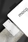 A business card with 'mocp' branding placed on a concrete surface, accompanied by a modern electronic device displaying the same text. The design is minimalist, featuring white and gray tones. A QR code is present on the card alongside the text 'Personal Brand'.