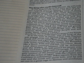 A close-up image of a page from a book or document, featuring English text printed in a block format. The text is densely packed with paragraphs and headings in bold, indicating different sections. The paper is light-colored, and the text is black with a readable, standard font. On the left side, there is a margin with evenly spaced dotted lines.