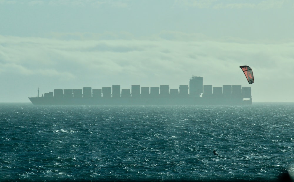 a person para sailing in the ocean with a large cargo ship in the background