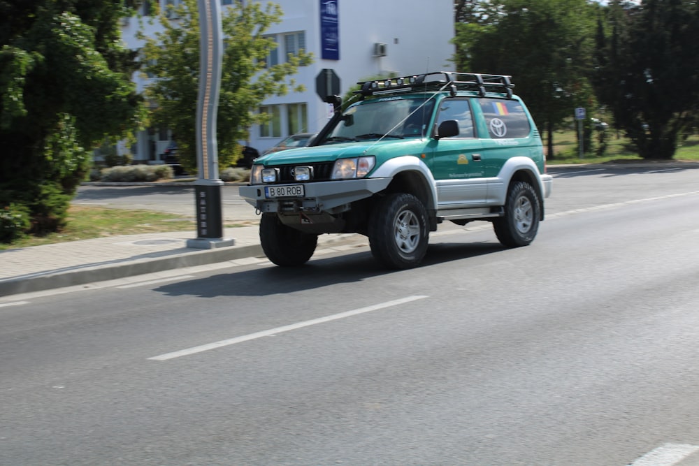 a green suv driving down a street next to a tall white building