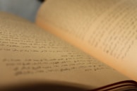 A close-up view of an open book with Arabic text. The pages are curved and the focus is on the middle of the book, with the background slightly blurred.