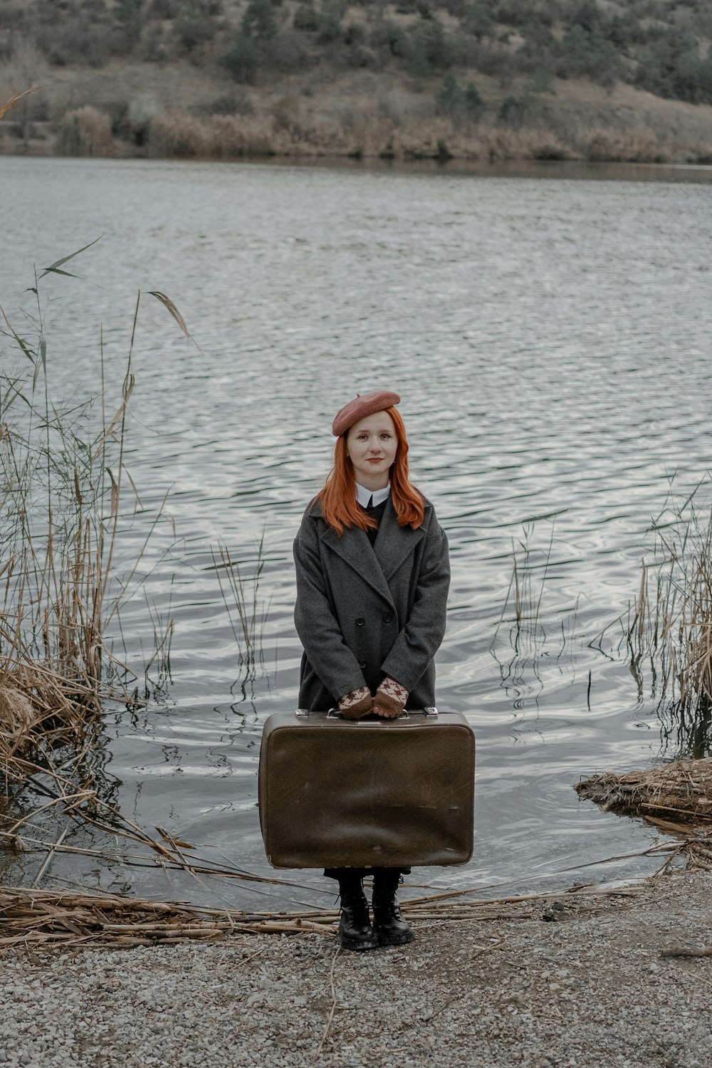 a woman with red hair is holding a suitcase by the water