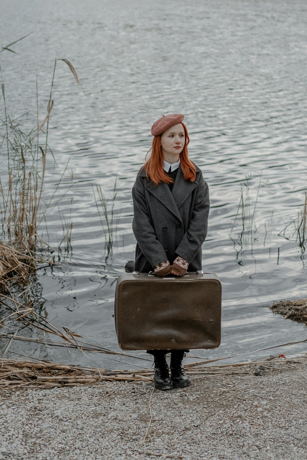 a woman with red hair is holding a suitcase by the water