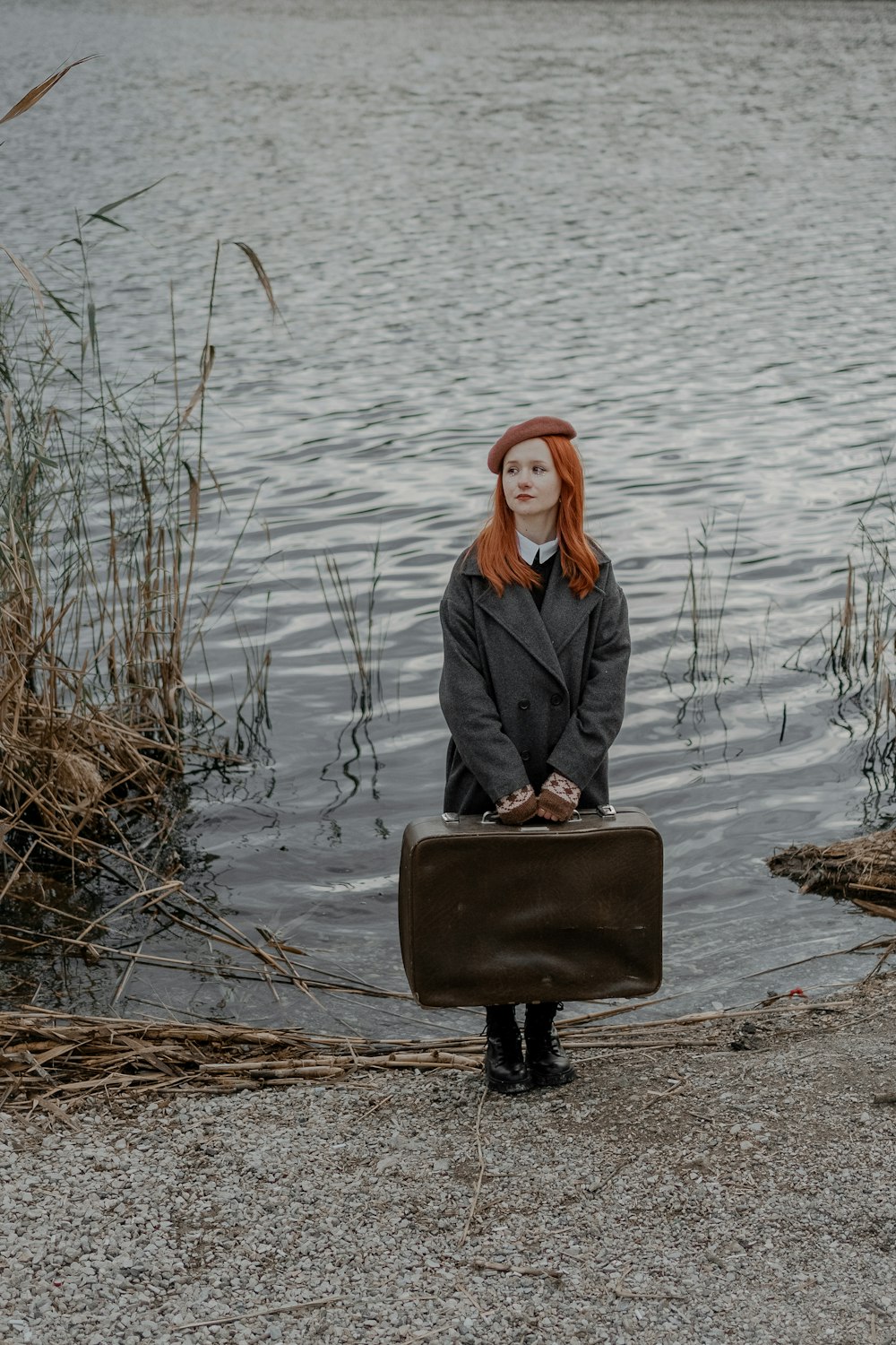 a woman with red hair is holding a suitcase by the water