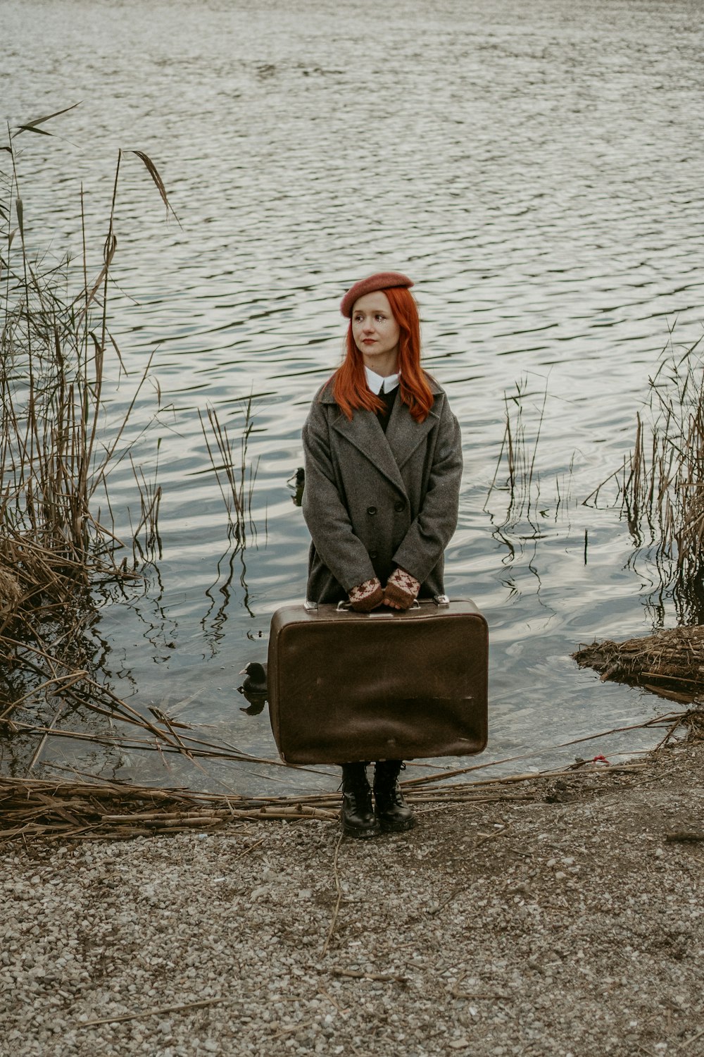 a woman with red hair is holding a suitcase by the water