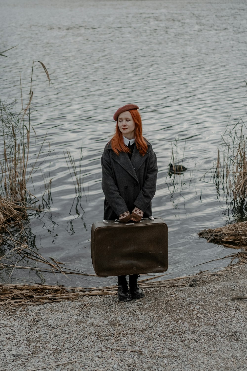 a woman with red hair is holding a suitcase by the water