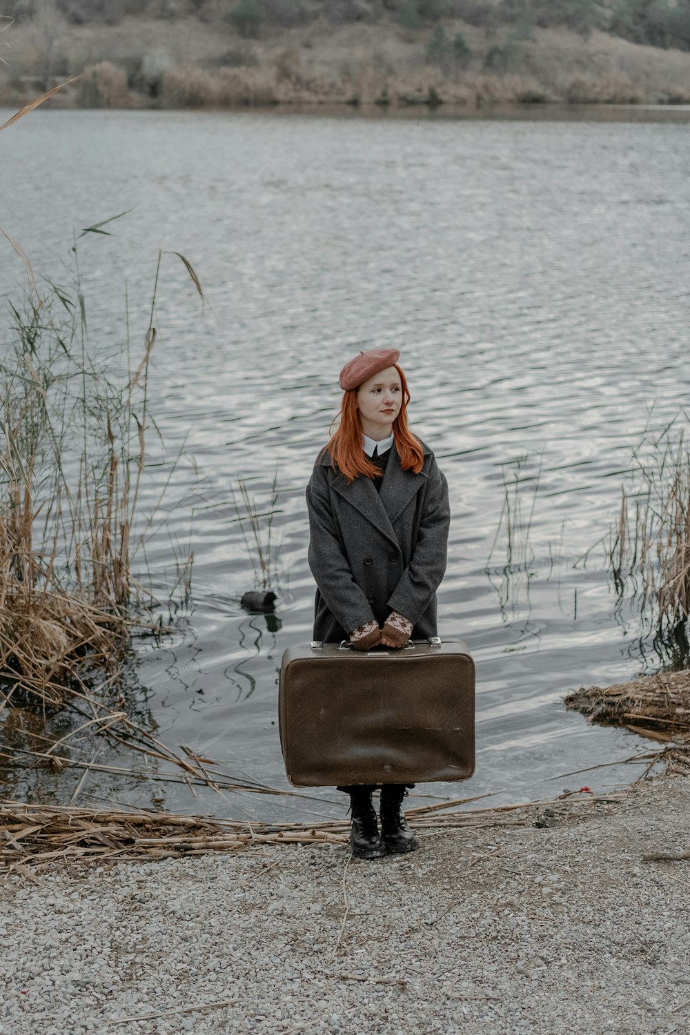 a woman with red hair is holding a suitcase by the water