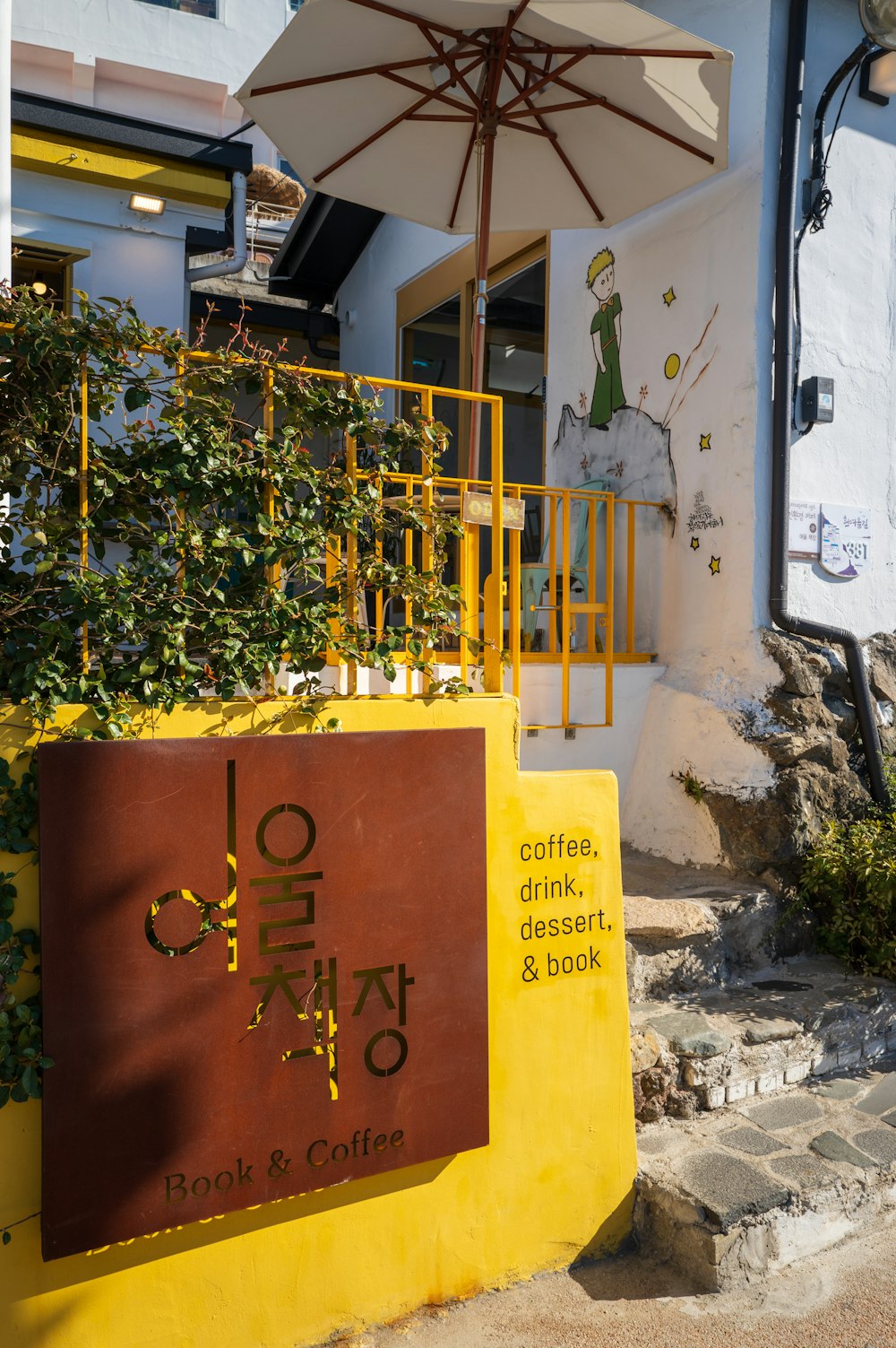 a yellow and brown sign and some plants and a building