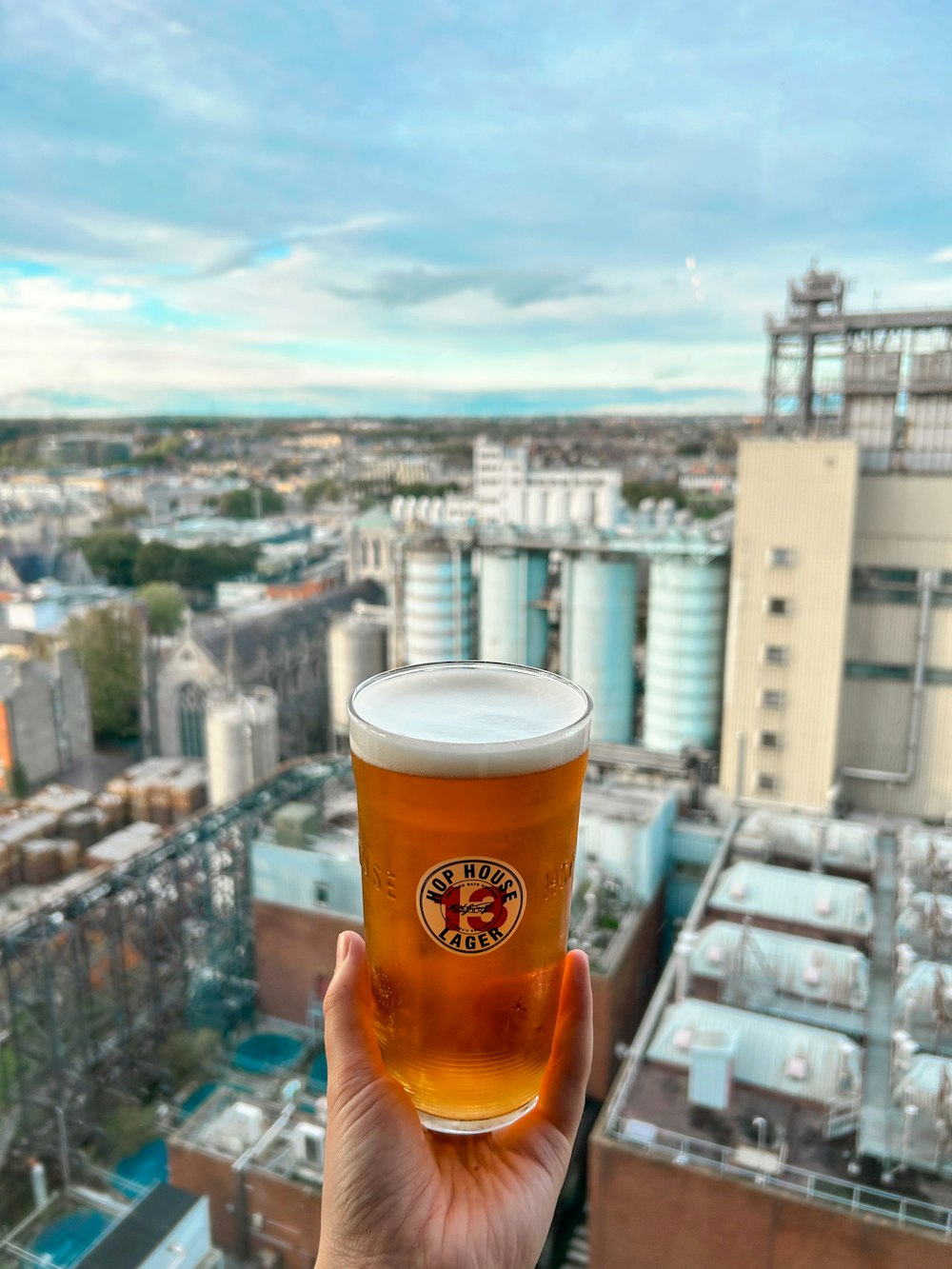 a person holding a glass of beer in front of a cityscape