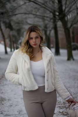 A stylish woman wearing a camel winter coat in a snowy park.