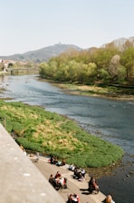 A vibrant view of families enjoying a sunny day by the riverbanks with lush greenery and walking paths.