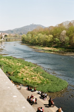 A vibrant view of families enjoying a sunny day by the riverbanks with lush greenery and walking paths.