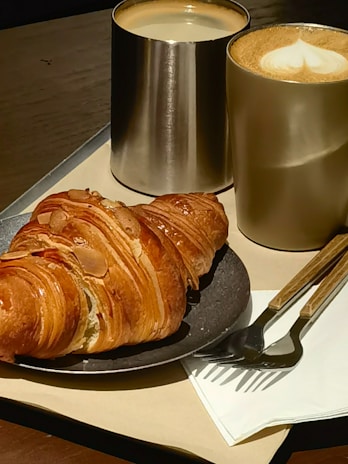 Artisan coffee cup with latte art served alongside a freshly baked croissant on a cream plate.