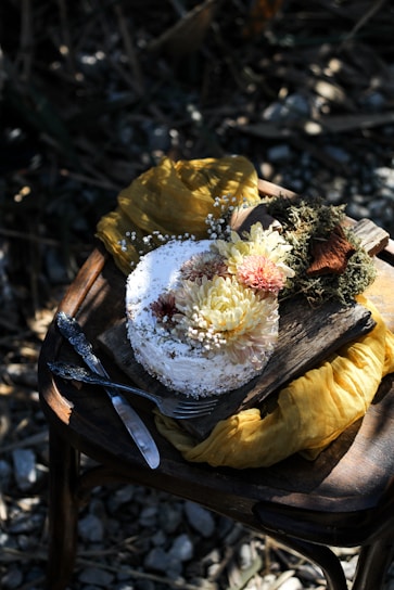 A rustic cake adorned with white frosting and delicate melon-colored flowers resting on a wooden table with a hint of brown ribbon.