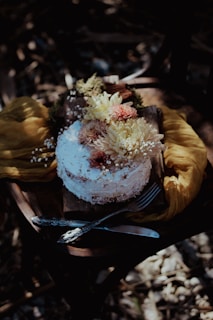 A rustic cake displayed on a wooden stand surrounded by flowers.