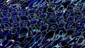 A complex pattern of abstract fluid shapes resembling liquid or molten metal, predominantly featuring smooth curves and glossy surfaces. The shapes are reflective, capturing hints of vibrant blue and black hues, creating a dynamic, energetic visual effect.