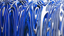 Abstract flowing patterns featuring glossy, elongated curves in blue and silver tones. The design creates a sense of fluid motion and depth, reminiscent of liquid metal.