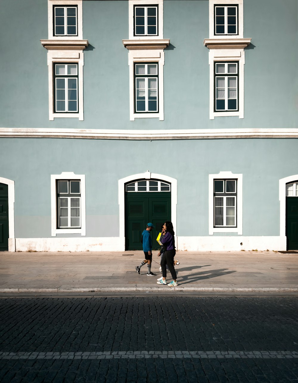 Dos personas caminando por una calle frente a un edificio azul