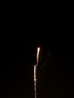 A close-up of a lit firework rocket ascending, trailing sparks against the dark sky.