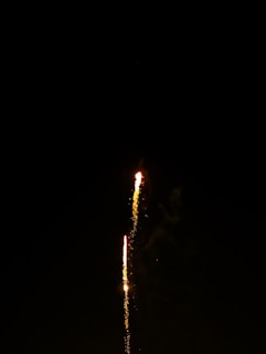 A close-up of a lit firework rocket ascending, trailing sparks against the dark sky.