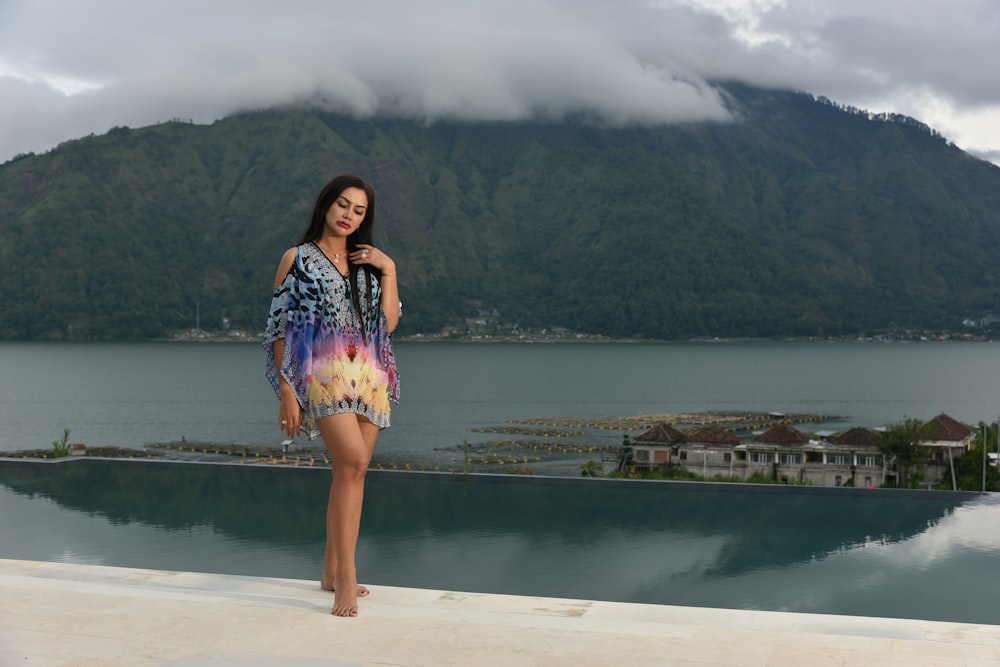 a woman standing on a ledge next to a body of water