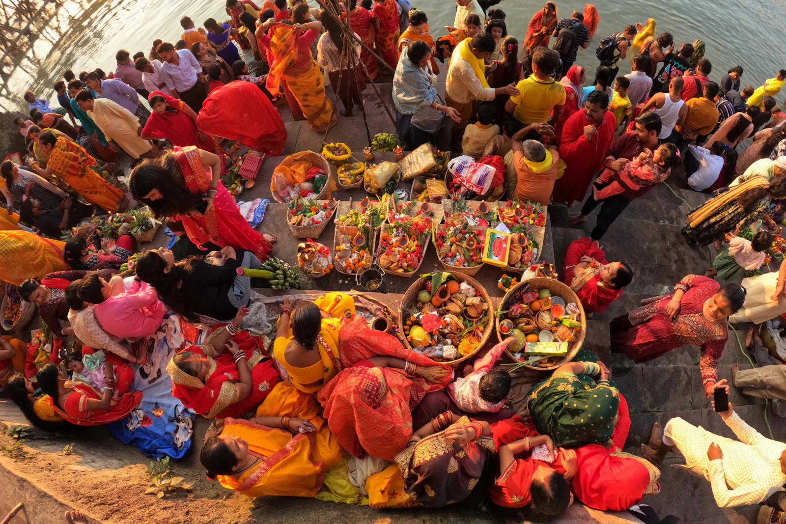 Devotees seated on a riverbank with baskets of fruit and offerings.
