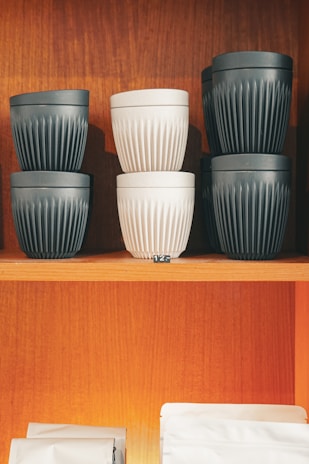 Stack of finished ceramic cups in earthy tones arranged neatly on a wooden shelf.