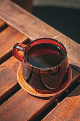 A steaming cup of dark coffee on a wooden table with morning light.