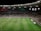 A soccer match is taking place in a large stadium filled with spectators. The scoreboard shows a score of 0:2, indicating that the away team is winning. Players are spread across the field, with a goalkeeper near one of the goals. The stadium is brightly lit and the stands are packed with fans.