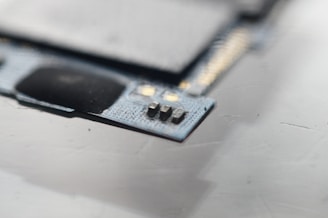 A close-up view of a circuit board with visible microchips and metallic components. The focus is on a small section of electronic components situated on a textured surface.
