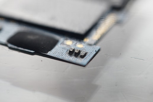 A close-up view of a circuit board with visible microchips and metallic components. The focus is on a small section of electronic components situated on a textured surface.