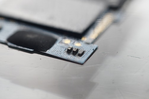 A close-up view of a circuit board with visible microchips and metallic components. The focus is on a small section of electronic components situated on a textured surface.