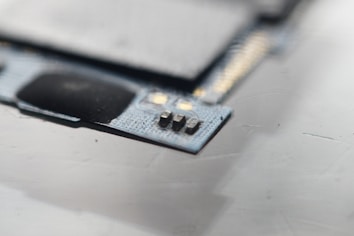 A close-up view of a circuit board with visible microchips and metallic components. The focus is on a small section of electronic components situated on a textured surface.