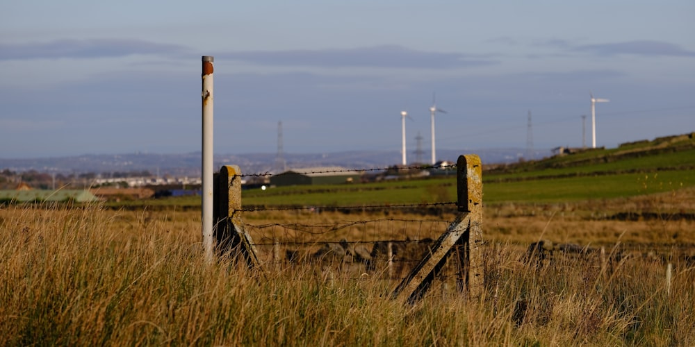 a gate in a grassy field with wind mills in the background