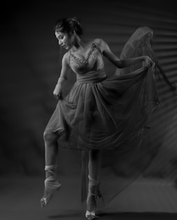 A ballerina poised gracefully, wearing a detailed, flowing dress. The soft lighting enhances the elegance and delicate textures of the fabric. The dancer's movement suggests a moment frozen in time, capturing her artistry and finesse.