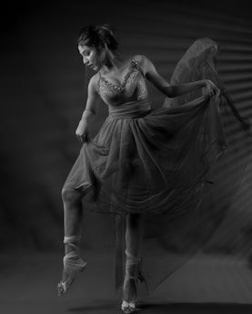 A ballerina poised gracefully, wearing a detailed, flowing dress. The soft lighting enhances the elegance and delicate textures of the fabric. The dancer's movement suggests a moment frozen in time, capturing her artistry and finesse.