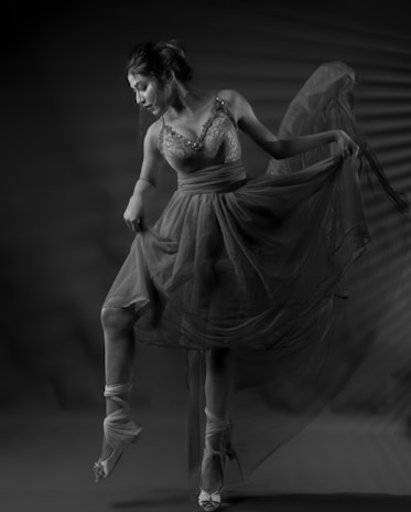 A ballerina poised gracefully, wearing a detailed, flowing dress. The soft lighting enhances the elegance and delicate textures of the fabric. The dancer's movement suggests a moment frozen in time, capturing her artistry and finesse.