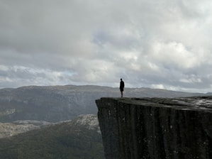 A person contemplating their future while sitting on a rocky cliff overlooking a vast landscape.