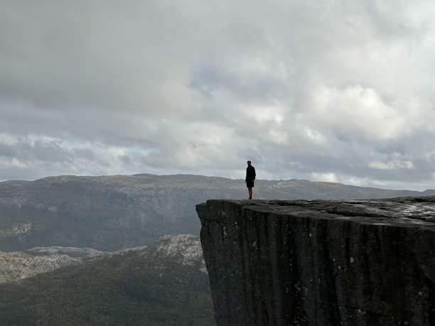 A person contemplating their future while sitting on a rocky cliff overlooking a vast landscape.