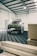 A rugged SUV with off-road modifications is parked inside a spacious industrial workshop. The vehicle has large tires and additional lighting mounted on the roof. The floor has a patterned surface, and wooden planks are stacked to one side.