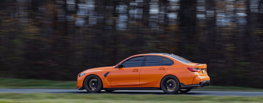 an orange car driving down a road next to a forest