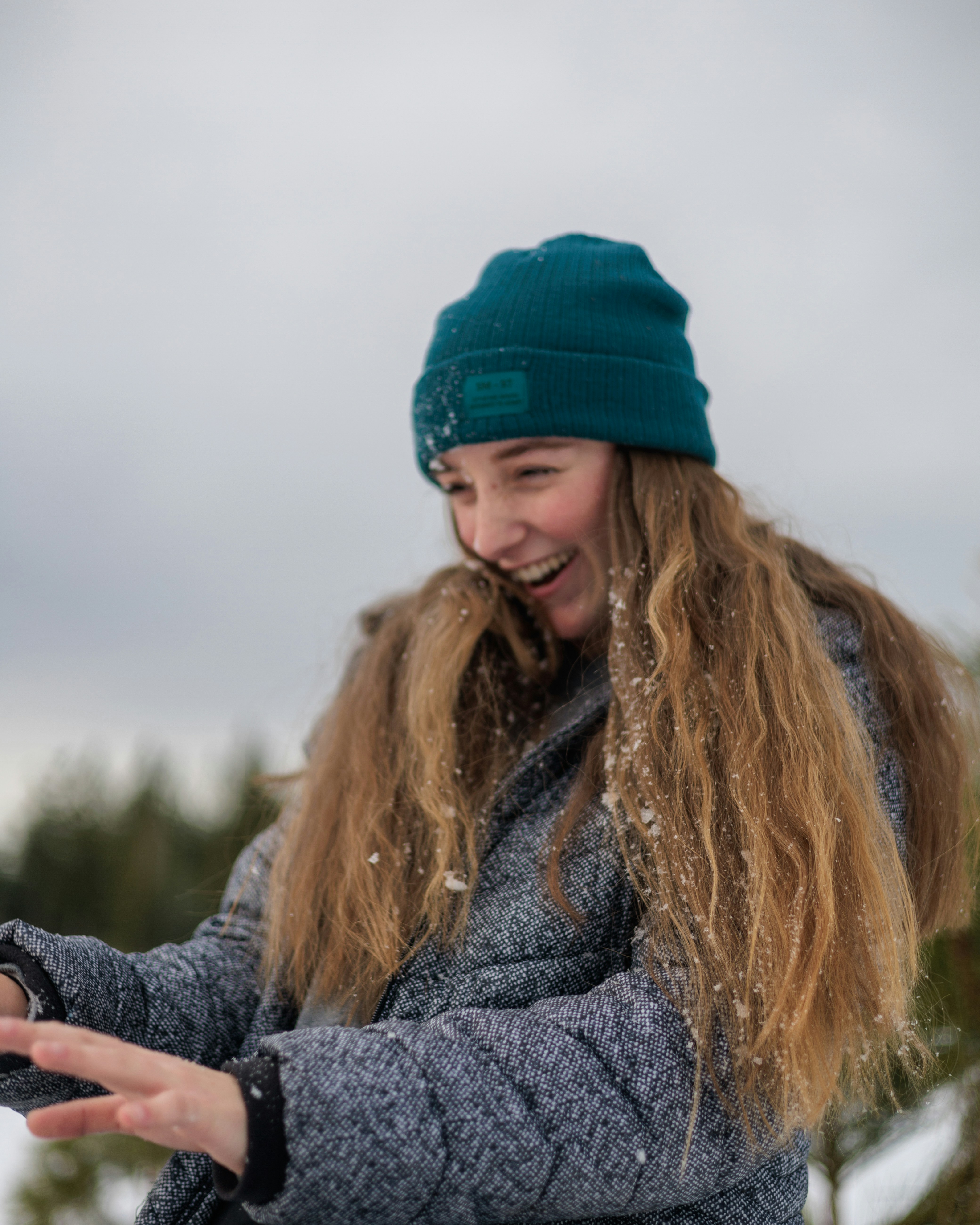 a woman in a blue hat and coat is throwing snow in the air