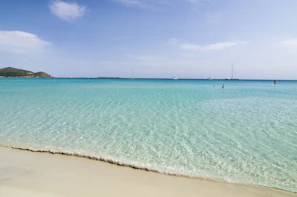 A serene beach scene with crystal clear turquoise water and a lone sailboat.