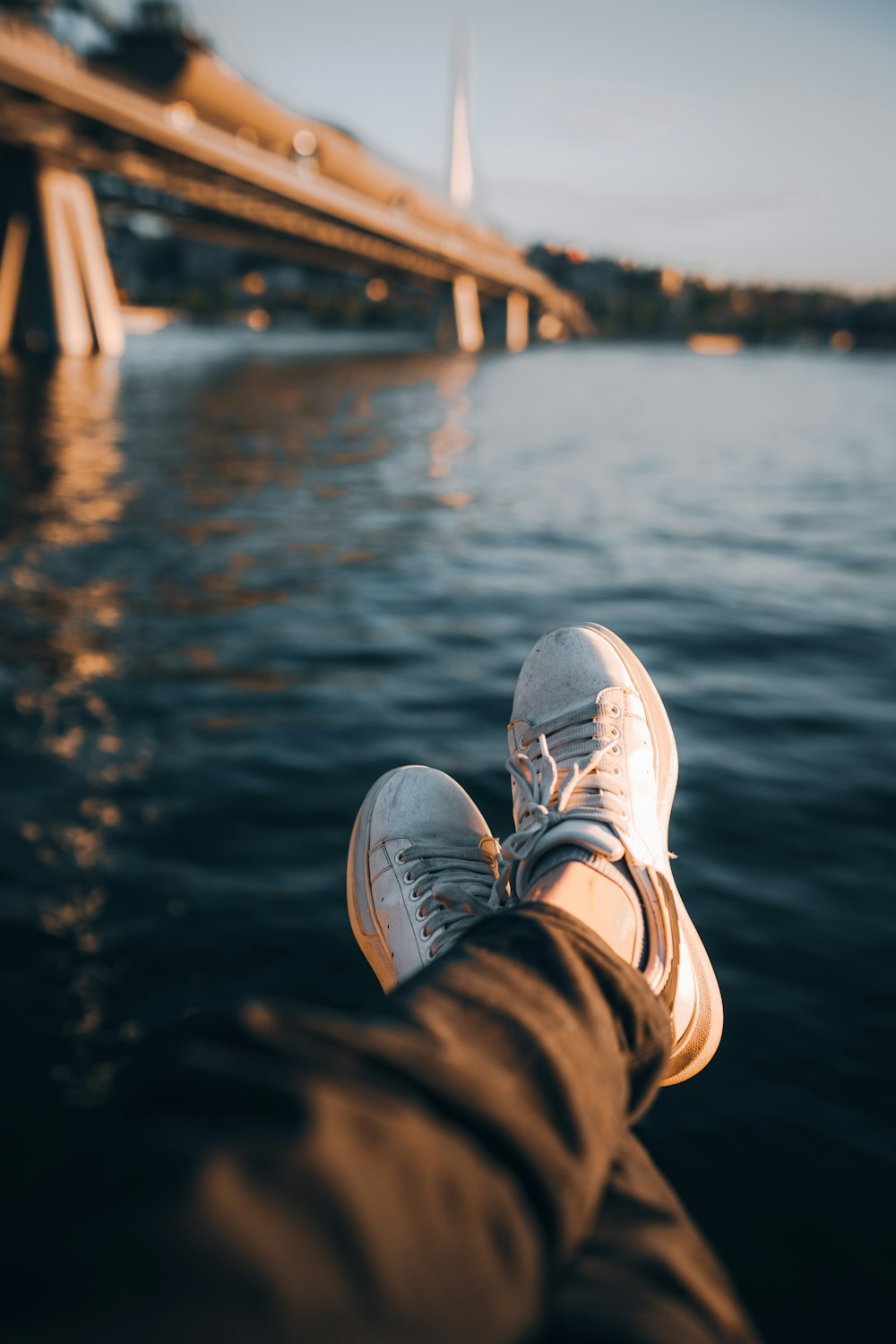 a person's feet sticking out of the water with a bridge in the background